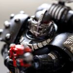 Close-up of a detailed miniature figurine of a sci-fi armored soldier in black armor with a red weapon and silver helmet, featuring intricate decorative markings.